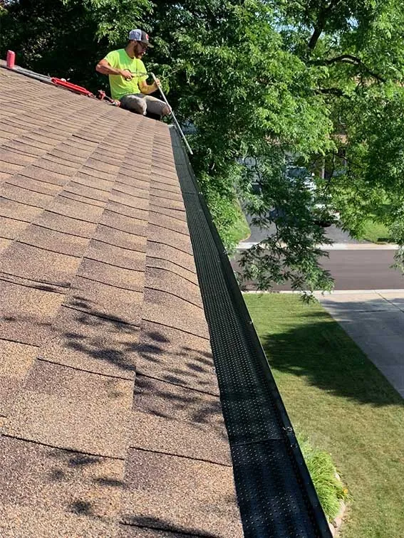 A New Summit Roofing crew member working on a gutter along the roof edge